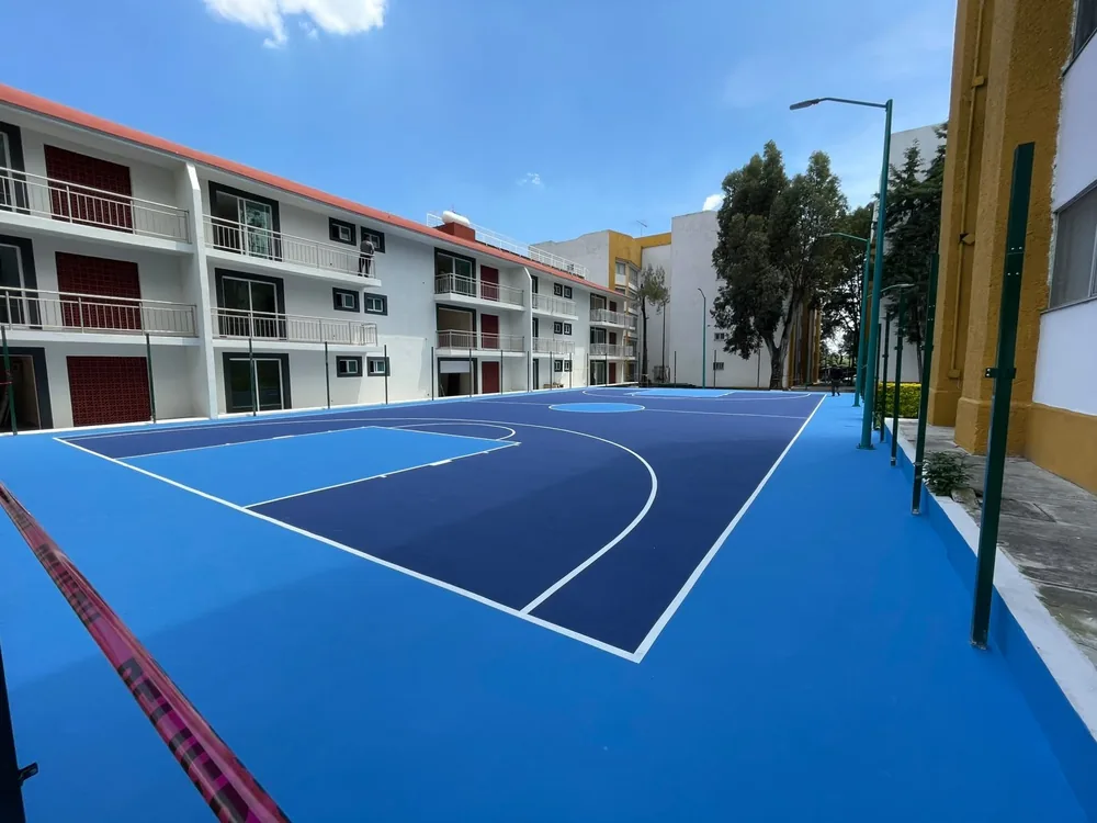 Vista lateral de la línea de tres puntos y la zona restringida blancas sobre piso acrílico azul antiderrapante de una cancha de basquetbol en Miguel Hidalgo, CDMX
